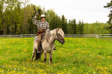 Cowgirl riding on horse (Icelandic horse). Green meadow and trees