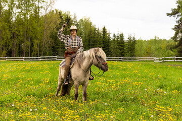 Cowgirl riding on horse (Icelandic horse). Green meadow and trees