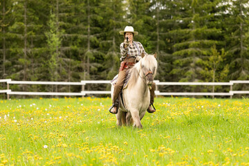 Cowgirl riding on horse (Icelandic horse). Green meadow and trees