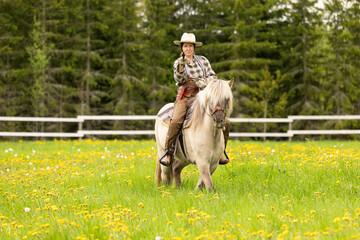 Cowgirl riding on horse (Icelandic horse). Green meadow and trees