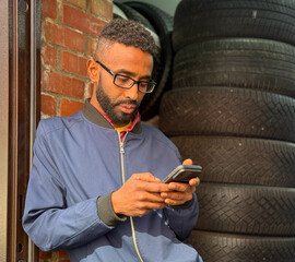 African-American man holds a mobile phone in his hands, typing a message and looks intently into...