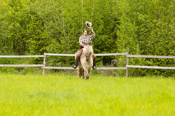 Cowgirl riding on horse (Icelandic horse). Green meadow and trees