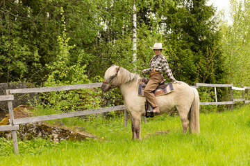 Cowgirl riding on horse (Icelandic horse). Green meadow and trees