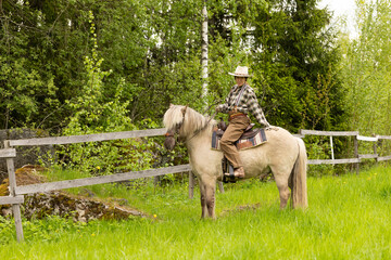 Cowgirl riding on horse (Icelandic horse). Green meadow and trees