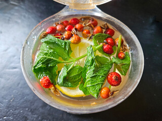 Looking down from directly above at the fresh ingredients of a healthy herbal tea made from lemon, mint and dried rose hips brewing in a plastic container.