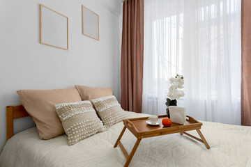 Cozy bedroom with a wooden breakfast tray on the bed, decorative pillows, and an orchid by the window.