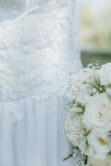 Close-up of elegant white wedding dress with floral lace details and bridal bouquet of white roses