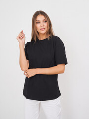 Woman posing in a casual black shirt and white pants against a minimal background