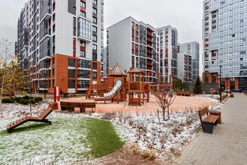 Play area with a wooden complex and benches in the courtyard of multi-story buildings, the ground is covered with light first snow.