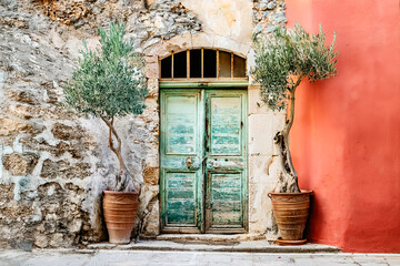 A lovely and picturesque green door beautifully framed by mature olive trees beside a rustic stone wall