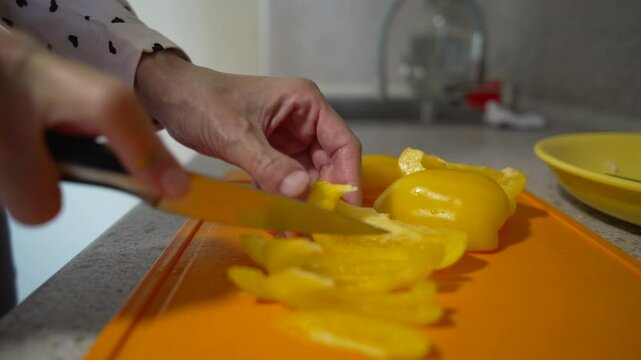 Pepper slicing kitchen Hand cuts yellow bell pepper on orange cutting board for meal preparation