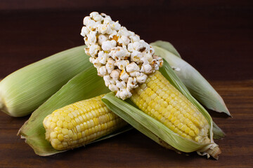 a couple of corn on a wooden table with corn grains and popcorn