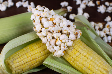a couple of corn on a wooden table with corn grains and popcorn with popcorns over around close