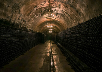 Dark underground wine cellar featuring endless rows of bottles illuminated by soft chandeliers