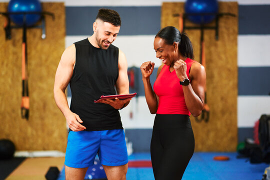 Personal trainer showing workout results on tablet to excited client in gym