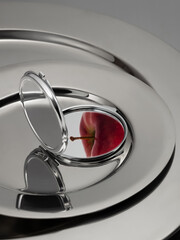 A red apple reflected in a round silver mirror lying on silver plates