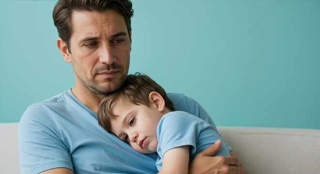 Concerned father comforting tired son in matching blue shirts against turquoise background. Father's day emotional support showing parental protection during difficult moments