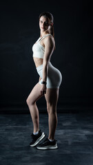 Athletic woman standing on black background, showing her fit body

