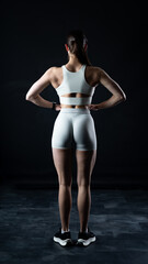 Obraz premium Athletic woman standing on black background, showing her fit body 