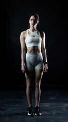 Obraz premium Athletic woman standing on black background, showing her fit body 