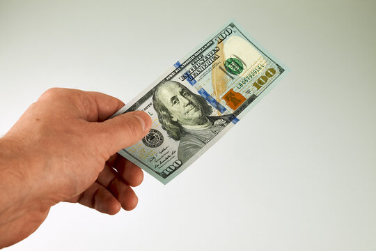 Male hand holding one new-design US $100 bill. Concept of payment, salary, cash transaction, finance, savings, investment.