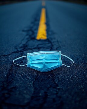 Discarded face mask lying empty street trampled forgotten symbolizing end of era macro shot ultra sharp detail high contrast between rough asphalt soft mask fabric cinematic moody lighting hyper