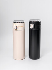 Two beige and black thermo mugs narrow cylindrical shape on white background