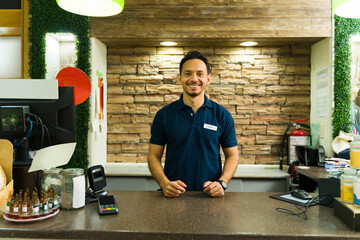 Smiling cashier waiting at checkout counter in grocery store