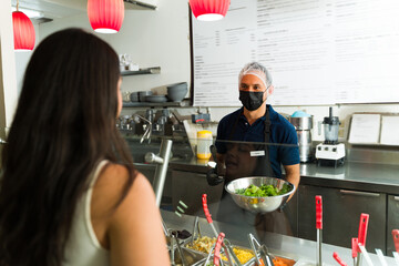 Restaurant worker serving customer fresh salad at salad bar