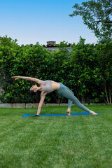 Fototapeta premium young woman yoga instructor doing exercice on mat on the grass