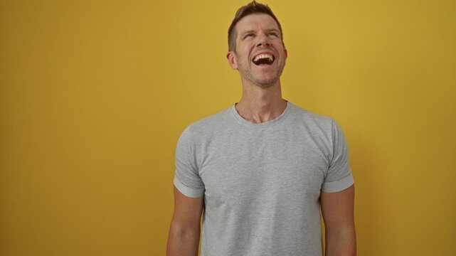 Young man yelling with joy against a vibrant yellow background, wearing casual grey t-shirt and expressing excitement with open arms.