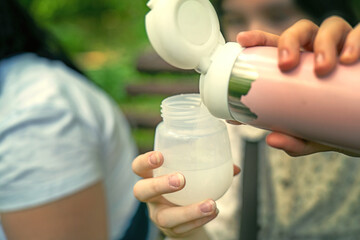 woman pouring warm water from a thermos into a baby bottle to prepare infant formula during a park outing