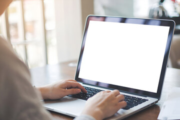 A close-up of a person's hands typing on a laptop with a blank screen, in a cafe setting.