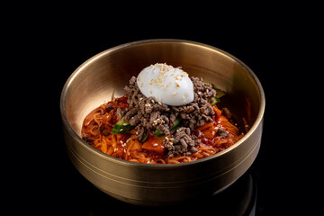 A vibrant bowl showcases spicy noodles mixed with fresh vegetables and tender ground beef. Atop rests a creamy soft-boiled egg, creating an appetizing visual delight on a dark backdrop