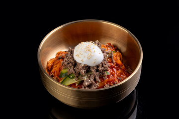 A vibrant dish features spicy noodles adorned with savory beef, fresh vegetables, and a creamy poached egg nestled on top. The striking golden bowl enhances the culinary delight