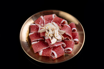 An elegant presentation of marbled beef slices is beautifully arranged on a shimmering golden platter. Fine garnishes enhance the gourmet appeal, inviting indulgence in a refined culinary experience