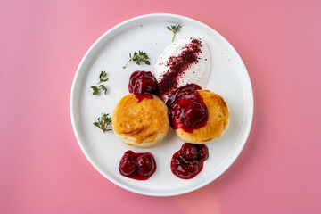 Soft, golden biscuits are generously adorned with rich berry compote and a dollop of creamy yogurt. The dish is beautifully presented on a bright pink plate, enhancing its appeal