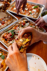 A lively weekend evening unfolds as friends eagerly grab slices of gourmet pizza, showcasing various toppings and flavors, surrounded by laughter and shared joy at the table