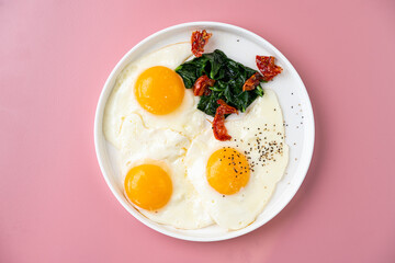 Three perfectly cooked sunny side up eggs sit alongside vibrant spinach and sun-dried tomatoes on a simple white plate, creating a colorful and appetizing breakfast display