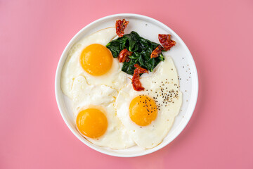Three perfectly cooked sunny side up eggs sit next to fresh spinach and garnished sun-dried...