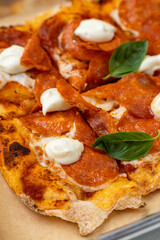 Golden crust pizza emerges from a handcrafted oven, adorned with perfectly melted cheese, spicy pepperoni, dollops of creamy sauce, and vibrant green basil leaves
