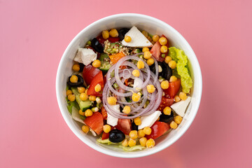 Vibrant bowl brimming with fresh salad ingredients such as lettuce, tomatoes, corn, onions, and black beans, artfully arranged and set against a bright pink backdrop, inviting healthy eating