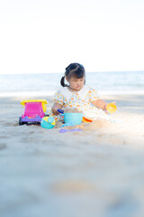 A little girl is playing in the sand on the beach,Happy fun Asian child cute little girl playing sand with toy sand tools at a tropical sea beach in holiday summer on sunset time, tourist trip concept