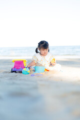 A little girl is playing in the sand on the beach,Happy fun Asian child cute little girl playing sand with toy sand tools at a tropical sea beach in holiday summer on sunset time, tourist trip concept