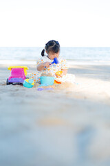 A little girl is playing in the sand on the beach,Happy fun Asian child cute little girl playing sand with toy sand tools at a tropical sea beach in holiday summer on sunset time, tourist trip concept