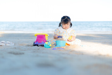 A little girl is playing in the sand on the beach,Happy fun Asian child cute little girl playing sand with toy sand tools at a tropical sea beach in holiday summer on sunset time, tourist trip concept