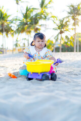 A little girl is playing in the sand on the beach,Happy fun Asian child cute little girl playing sand with toy sand tools at a tropical sea beach in holiday summer on sunset time, tourist trip concept