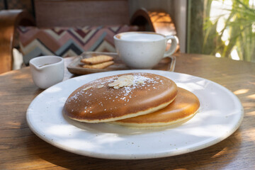 Tasty fluffy pancakes served with coffee and biscuits at a cozy cafe in the morning sunlight. Sweet homemade cakes on a white plate in close-up.