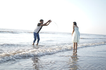 Happy young couple enjoying a romantic moment on a serene beach. The man lifts the woman joyfully while both smile and look relaxed