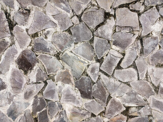 Rugged and uneven texture of a stone wall constructed from irregularly shaped, flat-faced stones....